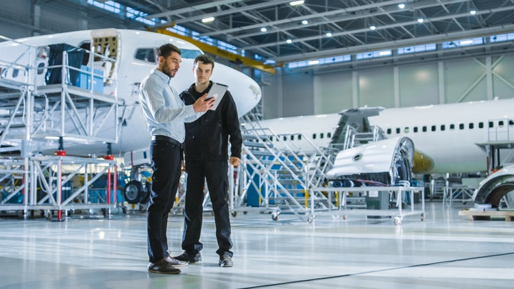 A personnel showing a tablet to another aircraft worker and explaining something in a hangar