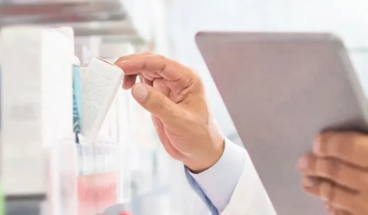 Closeup view of someone holding a tablet in one hand and picking out a package from a shelf with the other