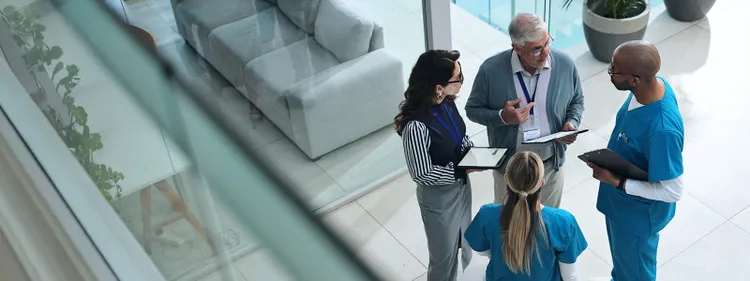 A group of healthcare professionals in scrubs engaged in conversation with each other in a clinical setting