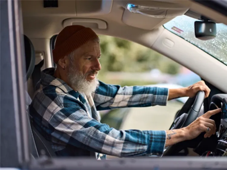 A man sitting in the driver seat of a car pressing buttons on the dashboard.