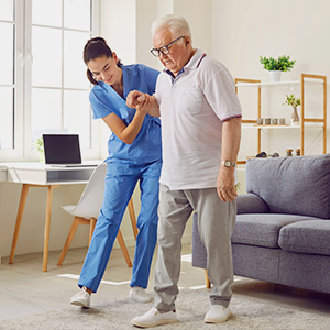 a nurse helping an old man to walk by holding his hand inside a room