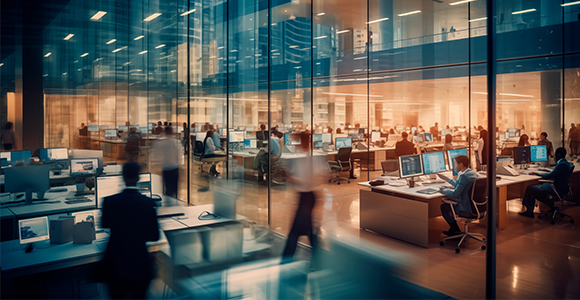 A blurred image of a office setting with multiple desks and employees going about their day.