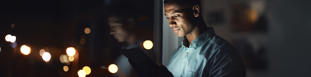 A man gazes at his phone, illuminated in a dark room, highlighting his focused expression.
