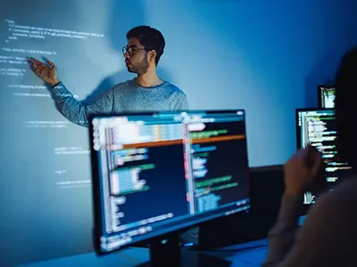 A young man making a presentation to participants sitting in front of their desktop computers