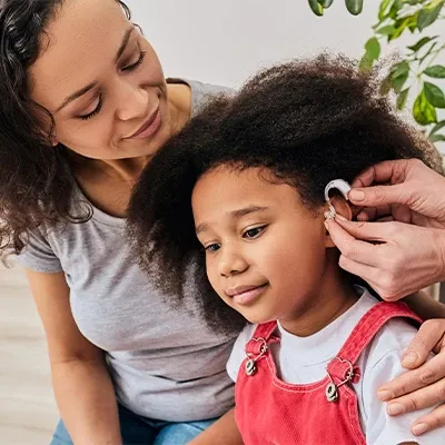 A woman helps a little girl with her hearing aid, showcasing a moment of guidance and connection between them.