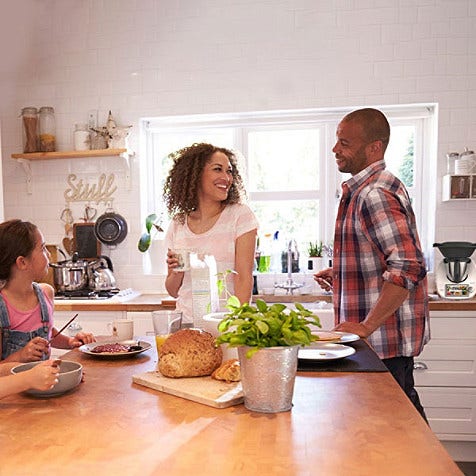 A happy family of four hanging around the kitchen table and talking.