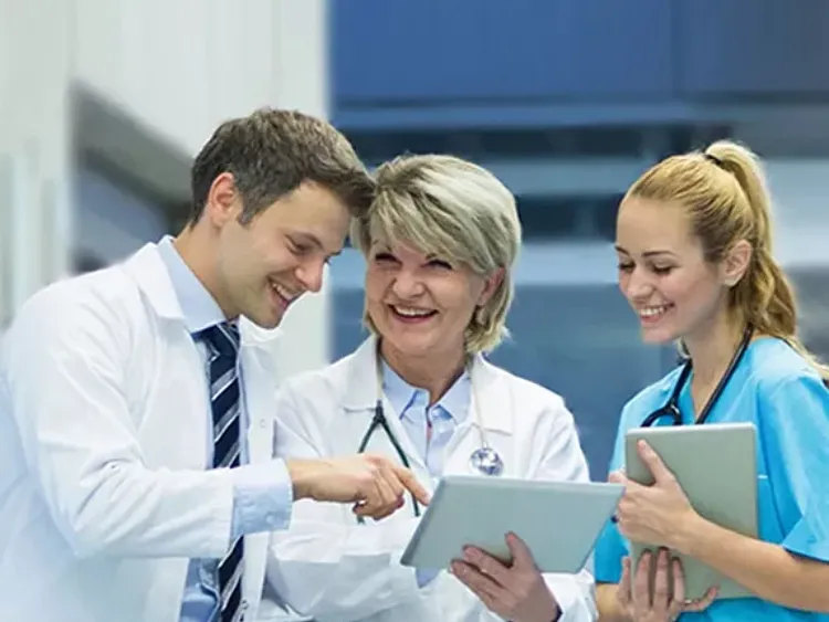 Three doctors and a patient examine a tablet together, discussing medical information in a clinical setting