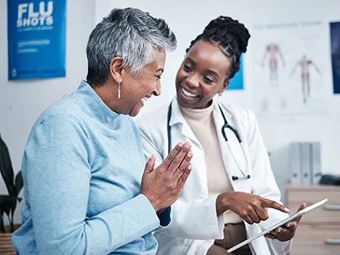 A doctor having a conversation with a woman holding a tablet, while they smile and talk