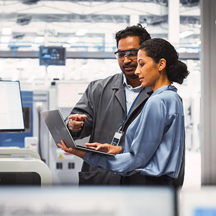 A male and female colleague having a conversation while looking at laptop screen.