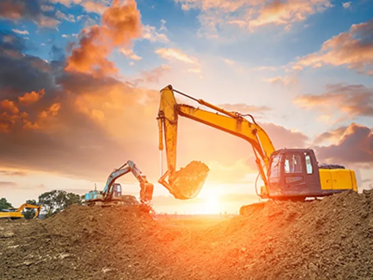 A bulldozer working in an open field with the sun behind it.