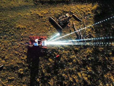 Aerial view of a tractor emitting a laser beam, highlighting its advanced agricultural technology in a field setting.