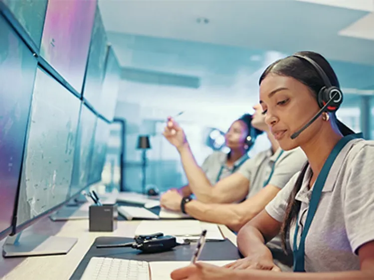 Employees wearing headphones sitting in a row at their workstations in from of their computers