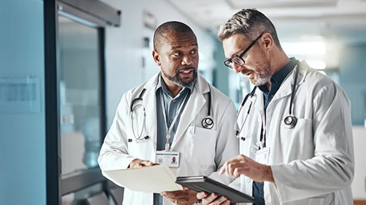Two doctors reviewing information on a tablet while standing in a hospital hallway
