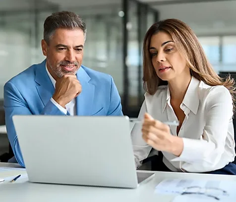 A healthcare legal professional pointing at a laptop screen explaining something to a another person sitting next to her.