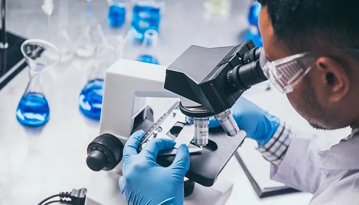 A man in a lab coat examines a sample through a microscope in a laboratory setting.