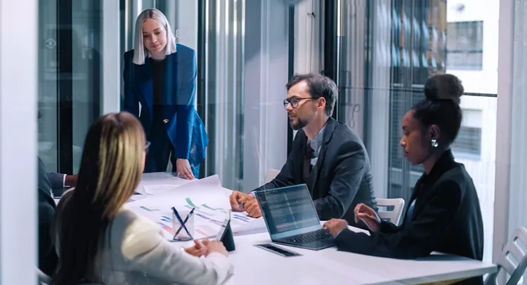 A group of four professionals in an office, intently discussing a complex digital diagram on a large screen.
