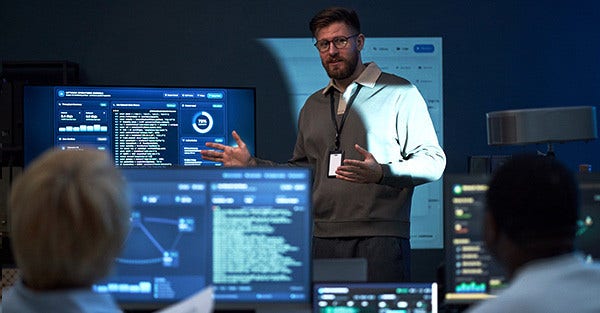 Two people collaborate in a modern server room with multiple monitors