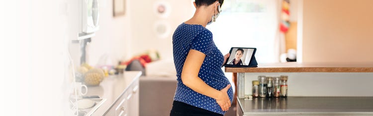 A pregnant woman engaging in a video conference with a health practioner on her laptop