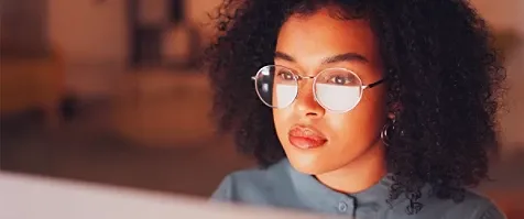 A young woman looking at a screen with the reflection on her spectacles