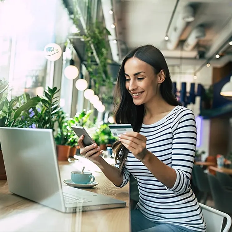 Woman looking at phone and bank card in cafe