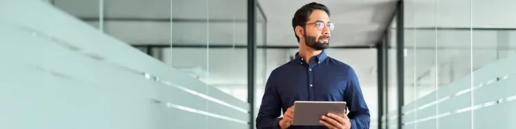A person holding a tablet and standing between office glass rooms