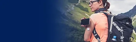 A woman carrying a heavy backpack, standing in an open, mountaneous landscape and holding her mobile phone