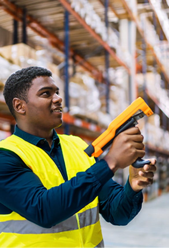 Warehouse employee, in a high-visibility safety vest, using a barcode scanner to track inventory in a retail distribution center.
