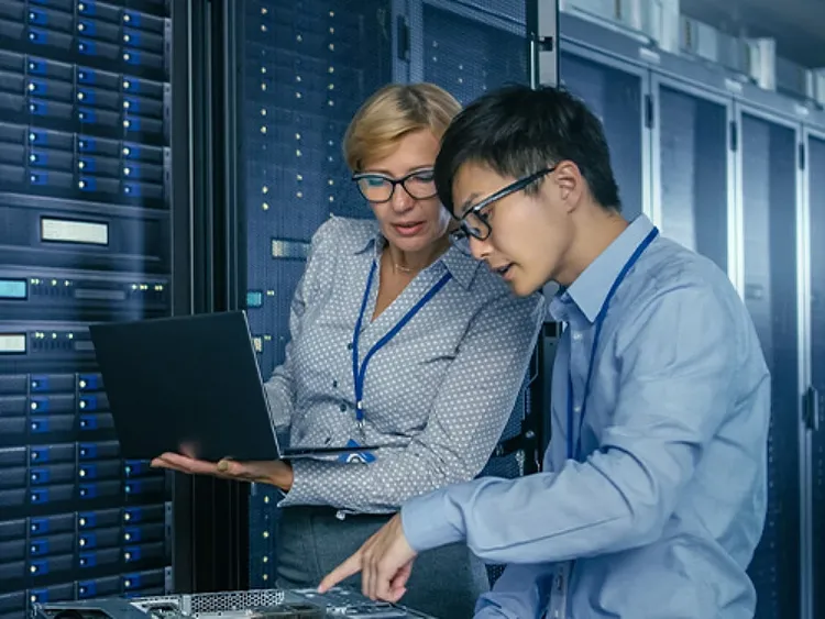 A male and female colleague having a conversation while standing by a row of data rack