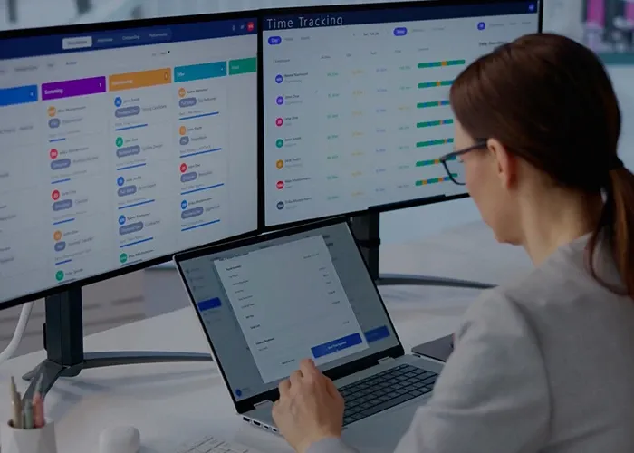 A woman looking into her laptop screen with two monitors behind the laptop