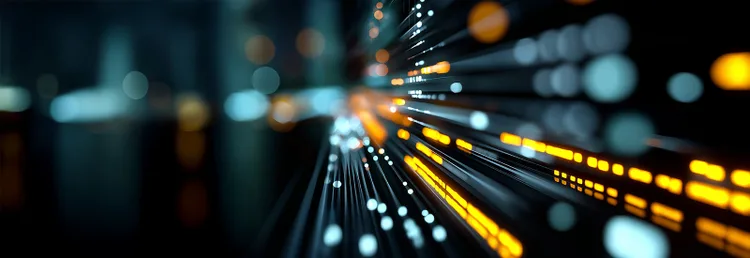 Abstract image depicting a network of glowing orange and white lights on dark background, resembling fiber-optic cables, conveying a sense of speed and technology.