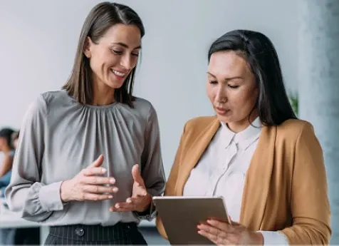 Two women standing next to each other discussing while looking at a tablet
