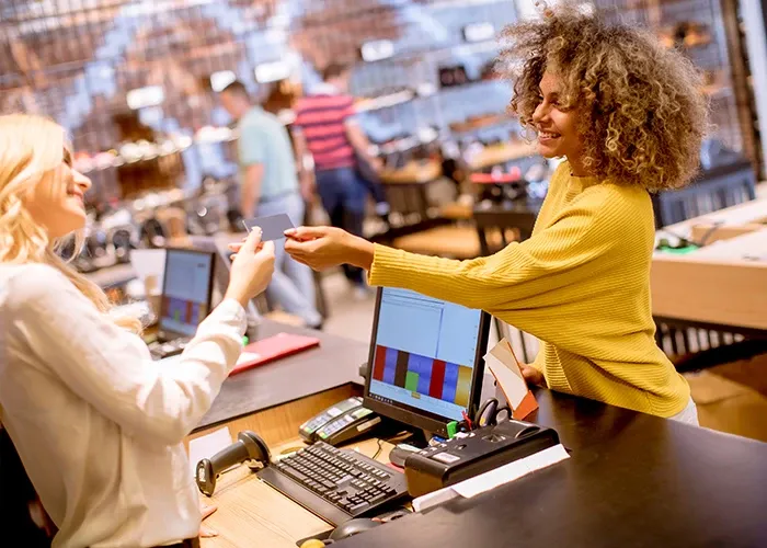 A smiling woman as a kiosk counter speaking to a cheerful cash lady