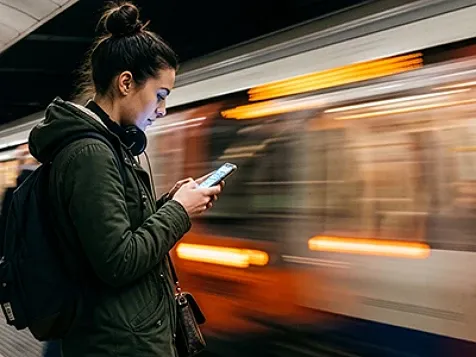 Woman using smartphone while subway train blurs past.
