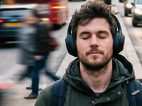 Man wearing headphones, eyes closed, amid city traffic.