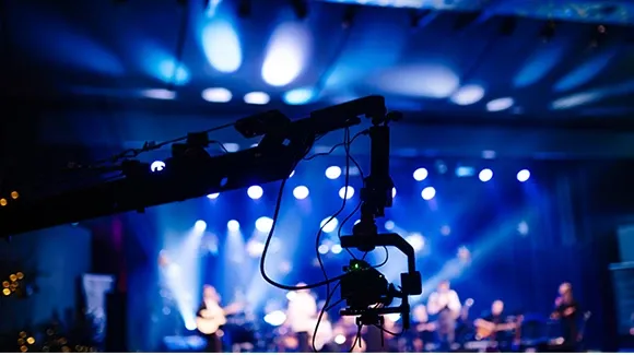 A camera is set up on a tripod, filming a performance on stage