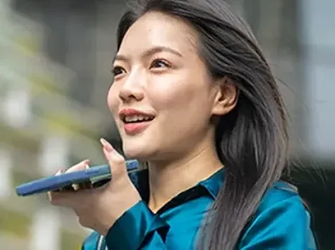 Woman speaking into smartphone outdoors using voice assistant.